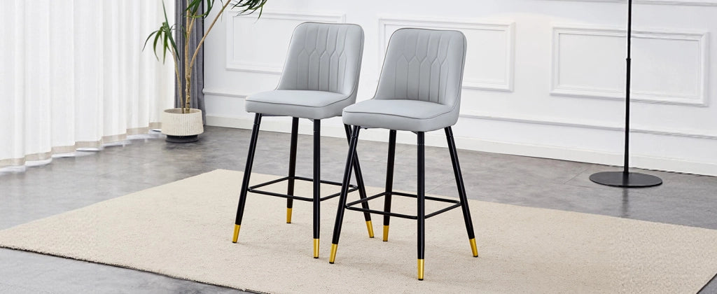 Set di due sgabelli da bar, alti 100 cm, realizzati in similpelle PU grigio chiaro con struttura in metallo nero e comodo poggiapiedi. Disponibili in